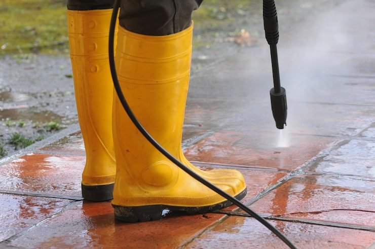 person-wearing-yellow-rubber-boots-with-high-pressure-water-nozzle-cleaning-dirt-tiles_181624-23652 pressure washing services in Australia